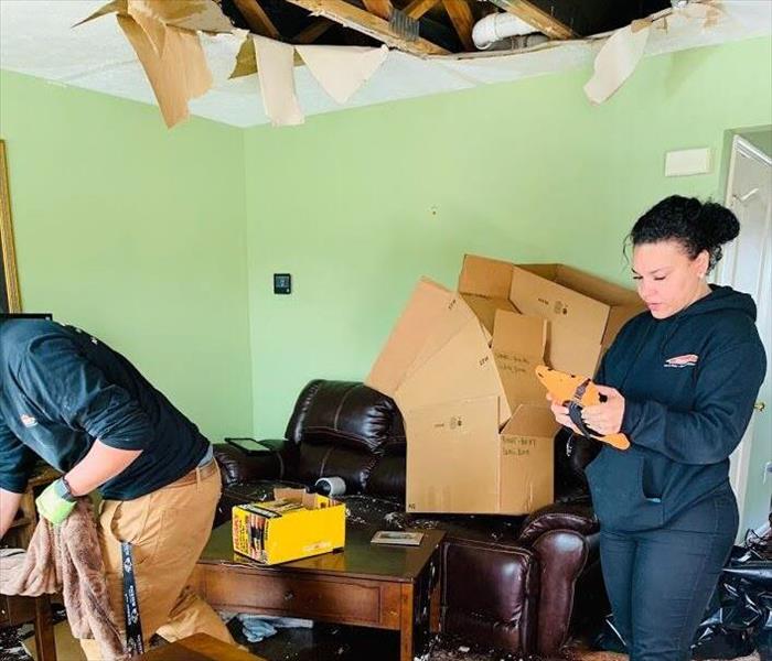 two Servpro workers reviewing restoration plans and cleaning water damaged ceiling debris